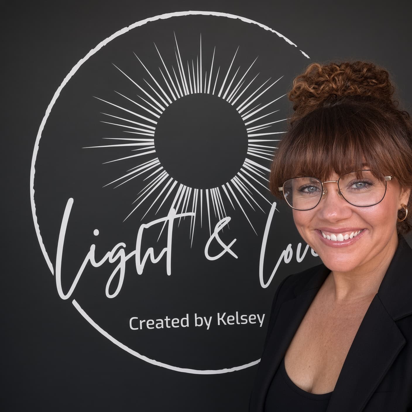 Kelsey Nelson, licensed esthetician and owner of Light & Love, smiling beside the studio’s script sunburst logo